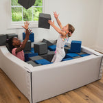 Two children playing with soft play blocks in a room with wooden flooring and large windows.