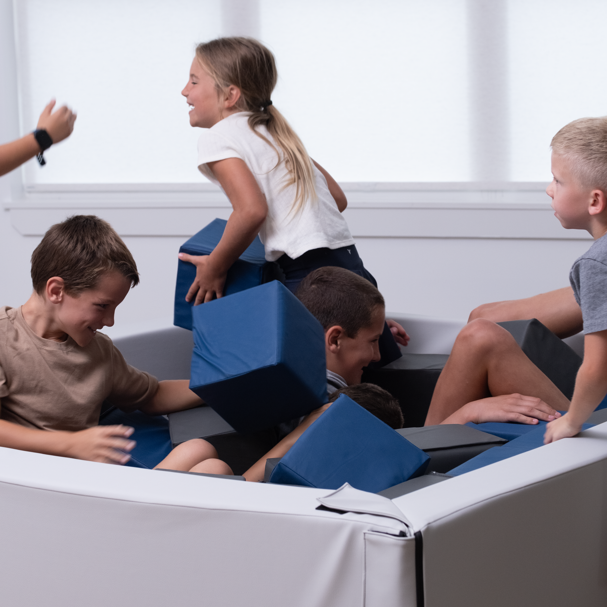 Children playing on a modern, white and blue play structure with large windows in the background.