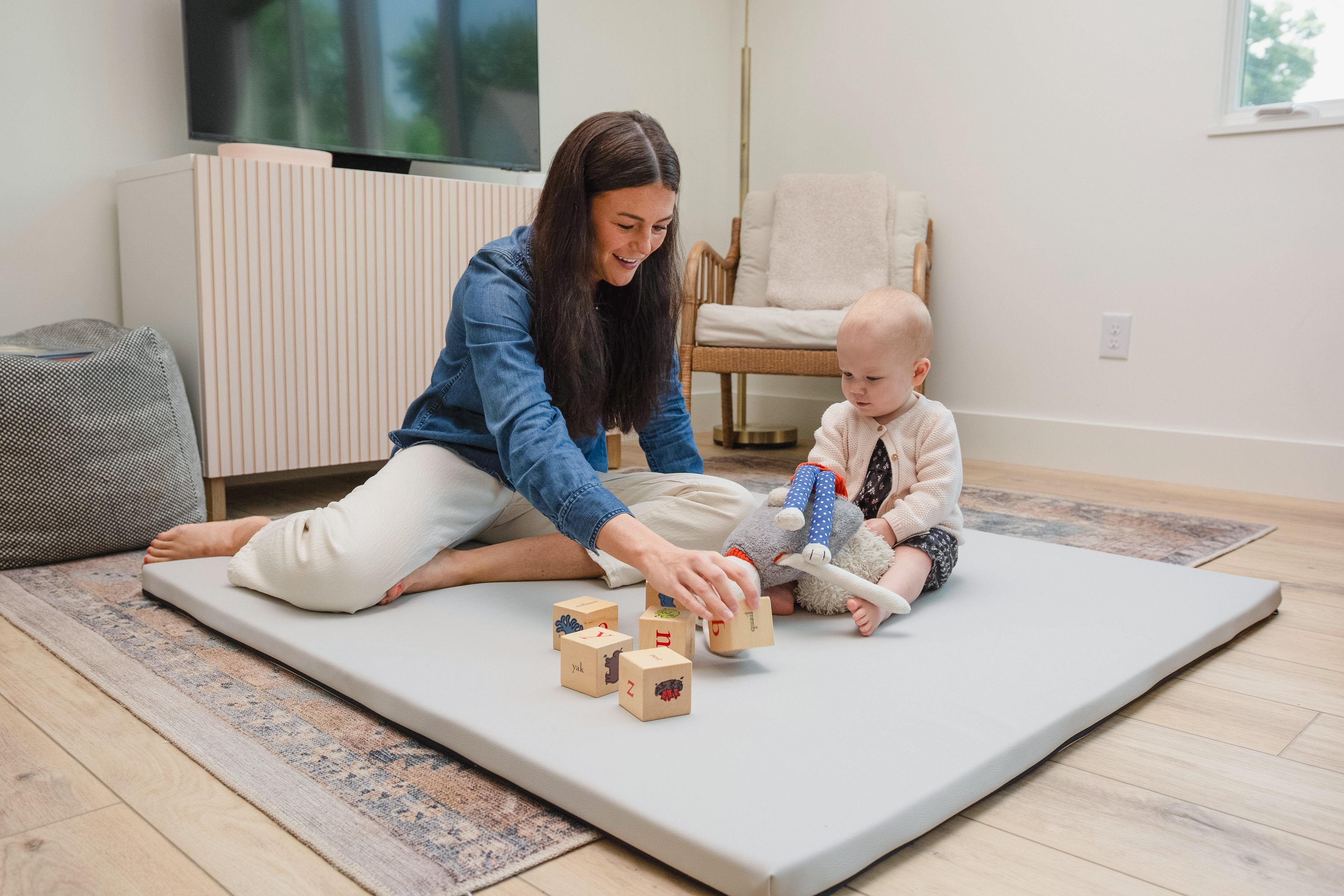 Woman and baby playing on a large mat with wooden blocks in a room.