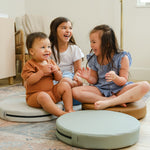 Lifestyle photo of three children laughing and sitting on Seagrass, Auster, and Nutmeg Roundabouts by Foamnasium.