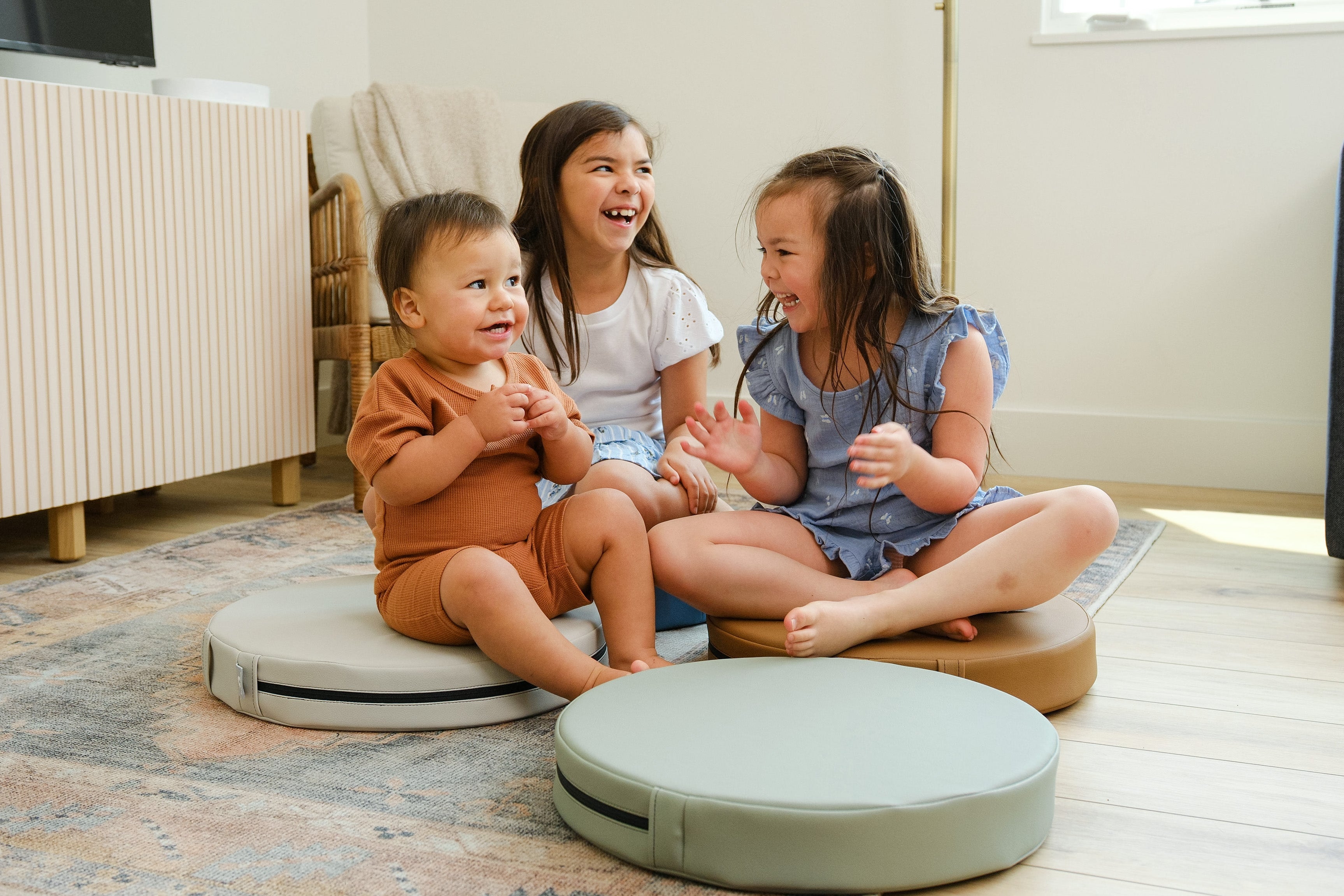 Lifestyle photo of three children laughing and sitting on Seagrass, Auster, and Nutmeg Roundabouts by Foamnasium.