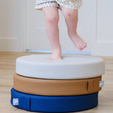 Lifestyle photo of toddler standing on a stack of Ink, Auster, and Nutmeg Roundabouts by Foamnasium.