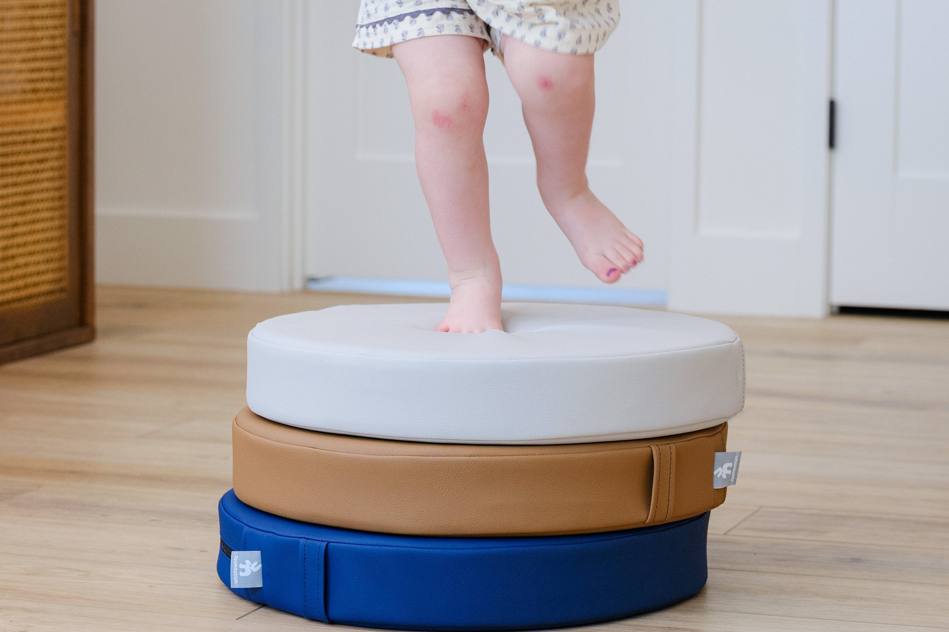 Lifestyle photo of toddler standing on a stack of Ink, Auster, and Nutmeg Roundabouts by Foamnasium.