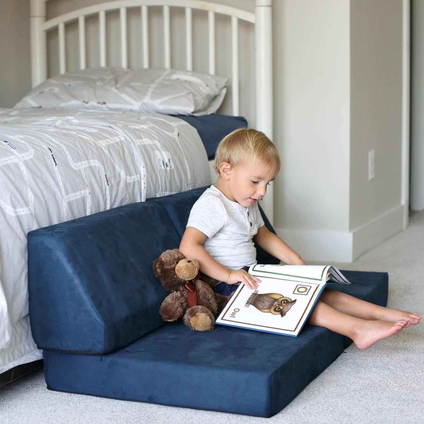 Lifestyle photo of a boy reading a book sitting on a Suede Navy Blocksy Mini by Foamnasium and Pottery Barn Kids