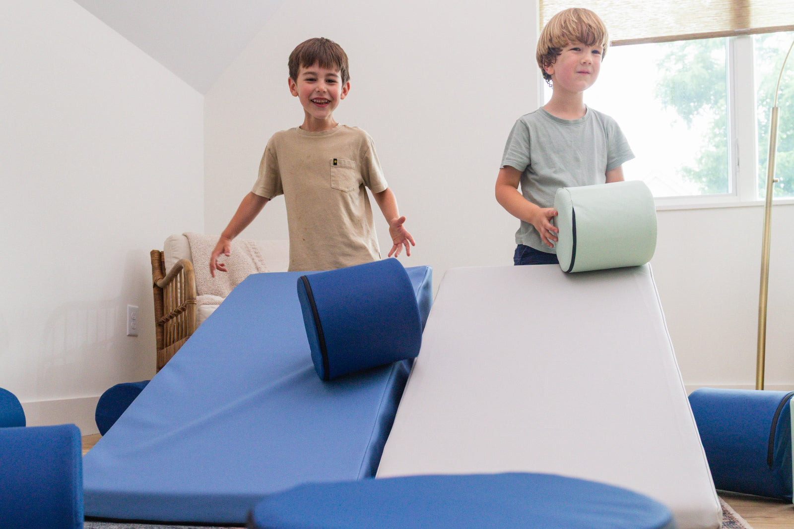 Two kids rolling foamnasium cylinders down mega wedges in living room 
