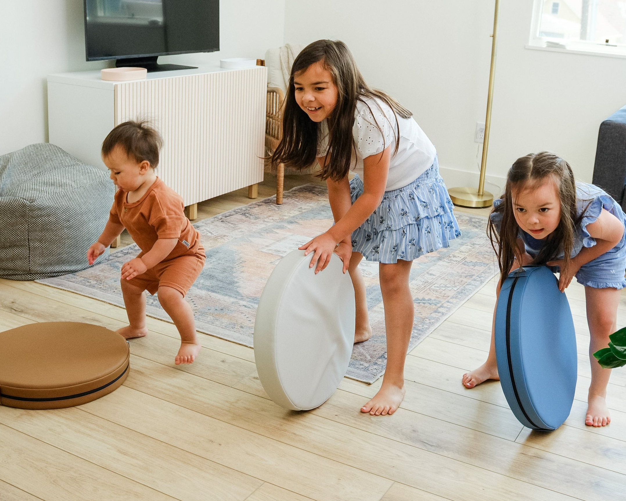 Three children playing with Foamnasium Roundabouts on a wooden floor in a living room.