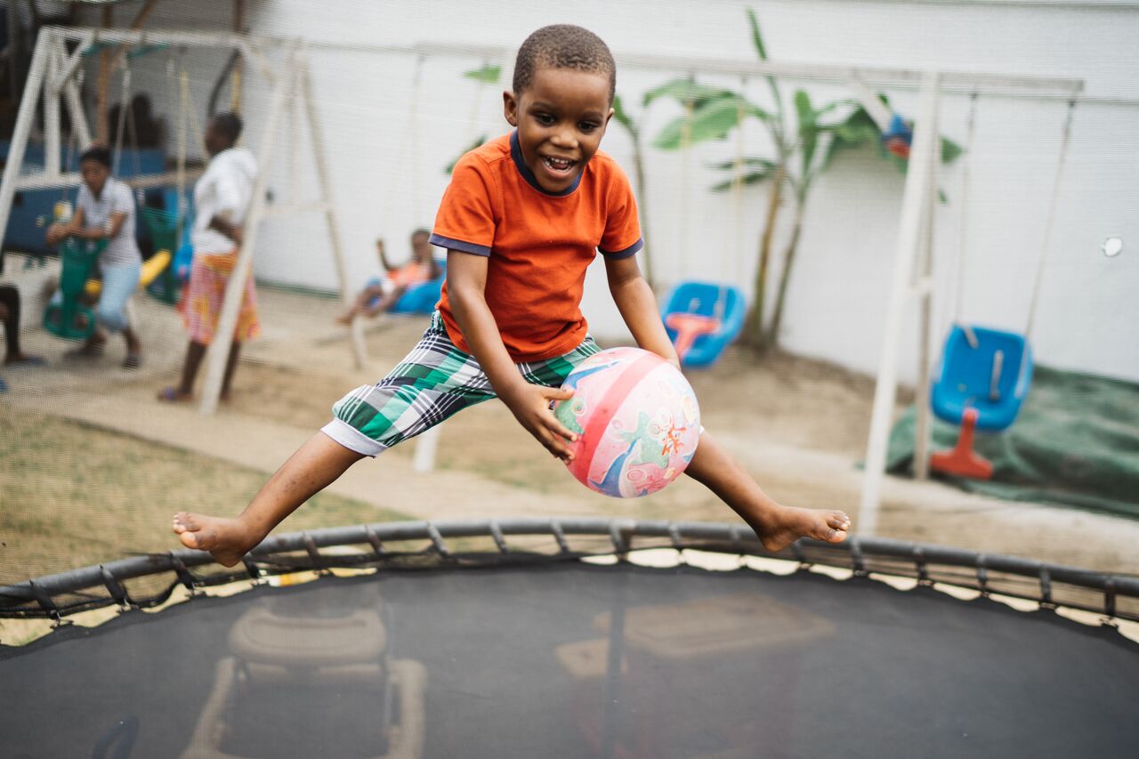 Photo of a boy jumping on a trampoline holding a ball at Mwana Villages