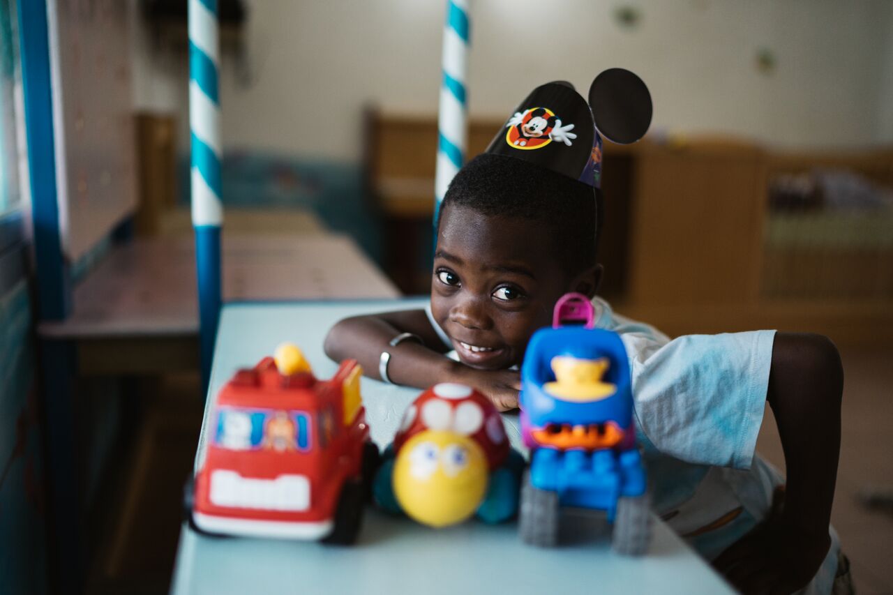 Photo of a boy smiling while playing with some toy cars at Mwana Villages