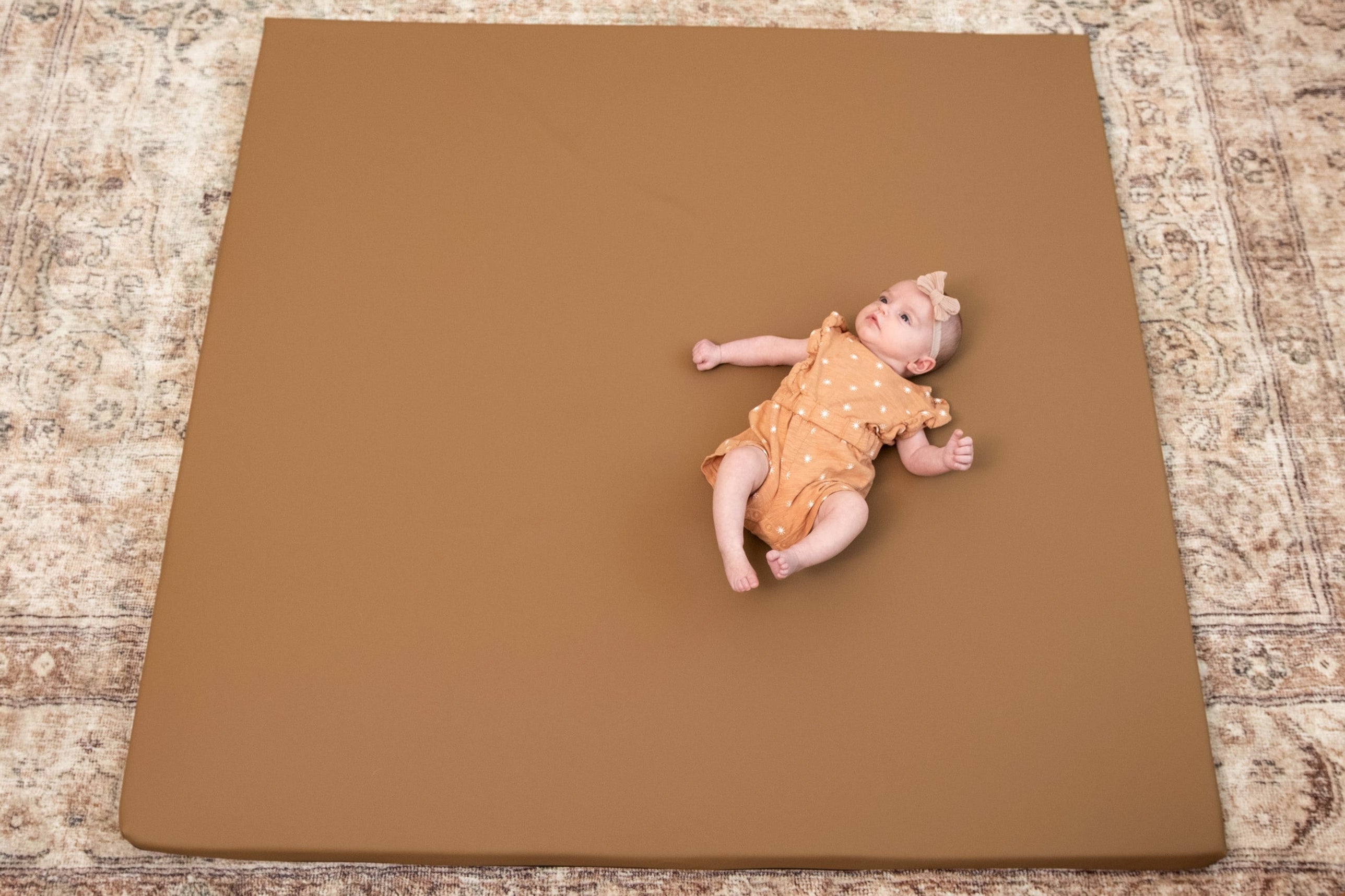 Baby lying on a Nutmeg Foamnasium mat on a patterned floor