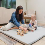 Woman and baby playing on a large mat with wooden blocks in a room.