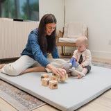 Woman and baby playing on a large mat with wooden blocks in a room.