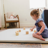 Child playing with wooden blocks on a mat in a living room.
