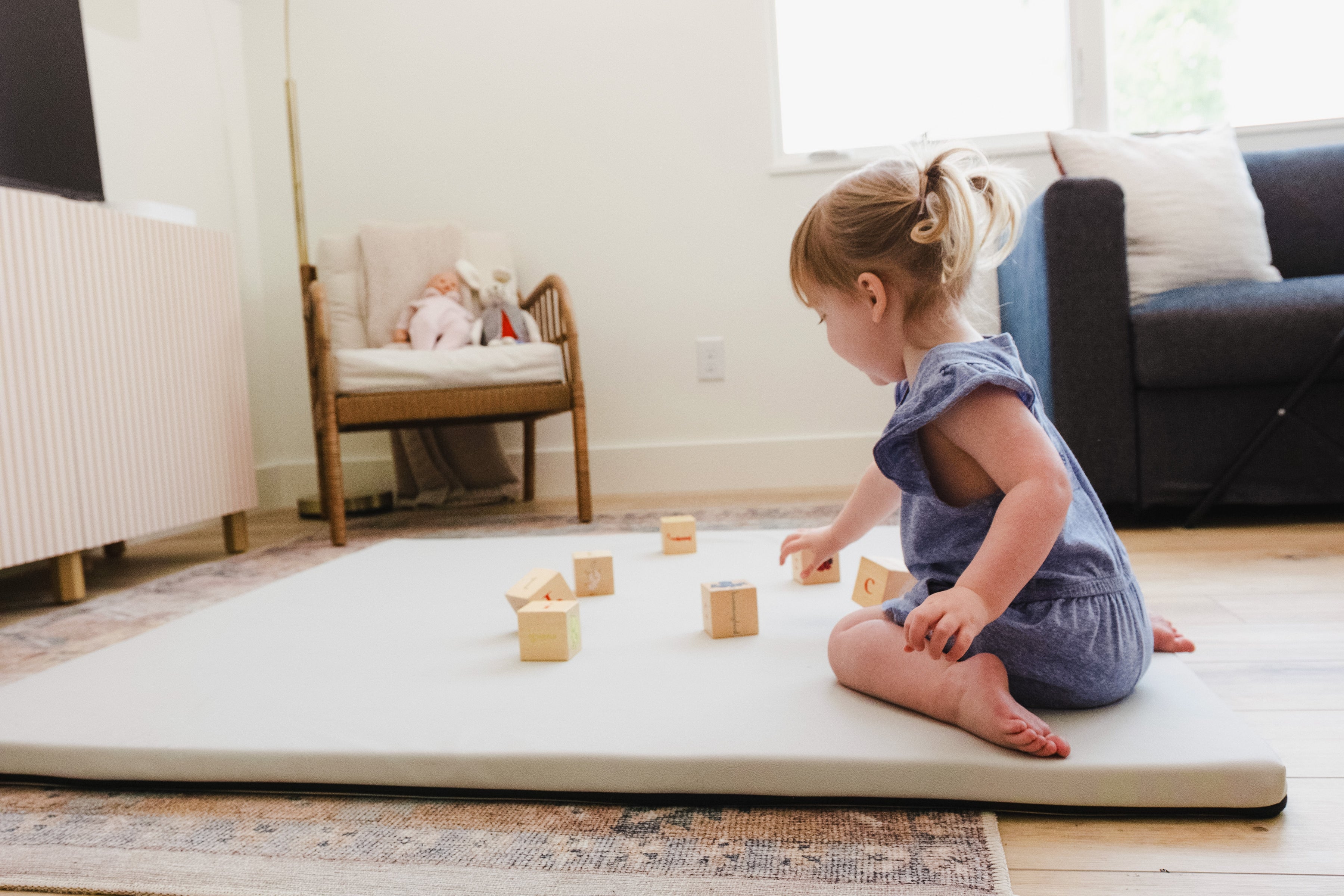 Child playing with wooden blocks on a mat in a living room.