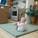 Baby sitting on a mat in a kitchen with toys around
