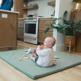 Baby sitting on a mat in a kitchen with toys around