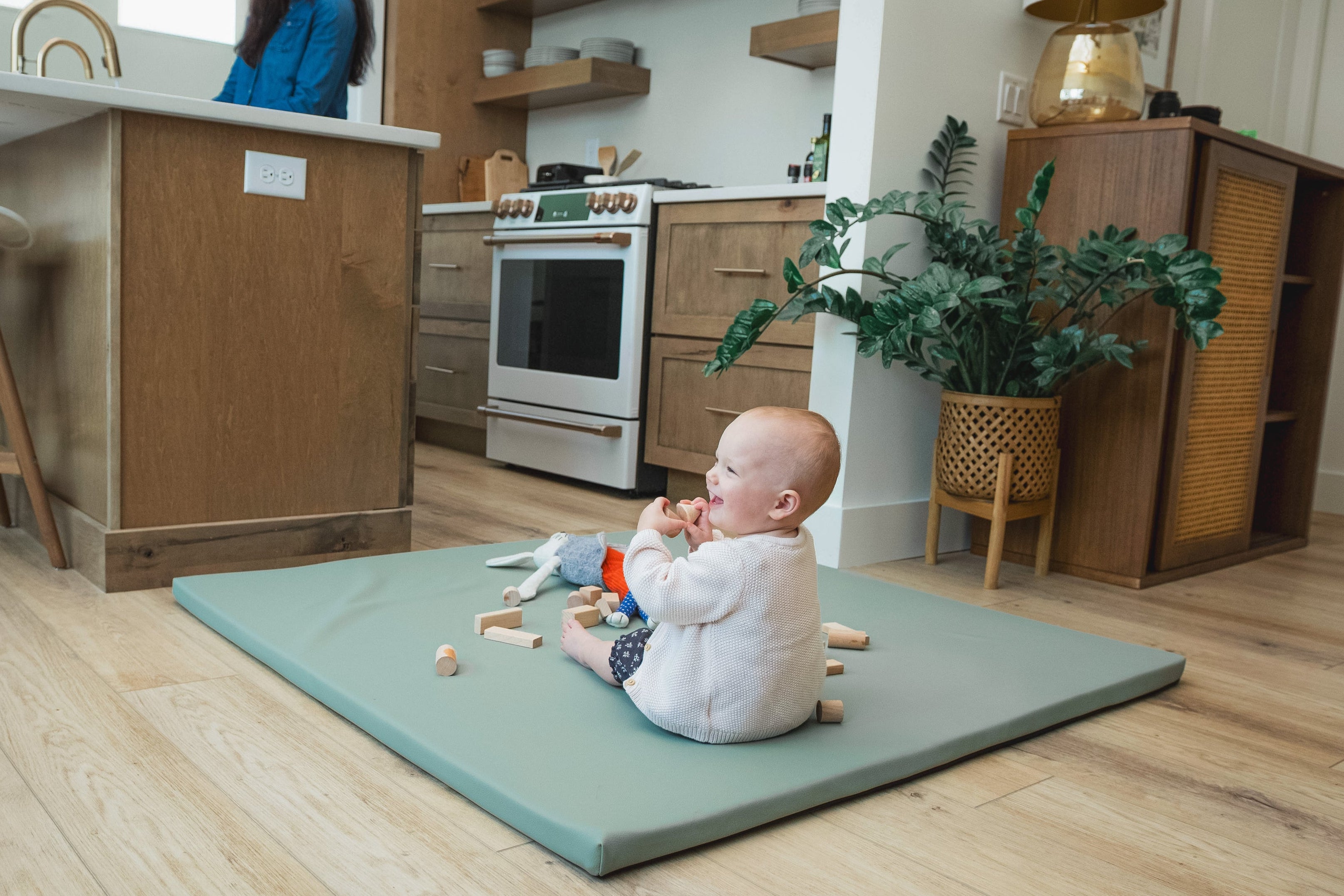 Baby sitting on a mat in a kitchen with toys around